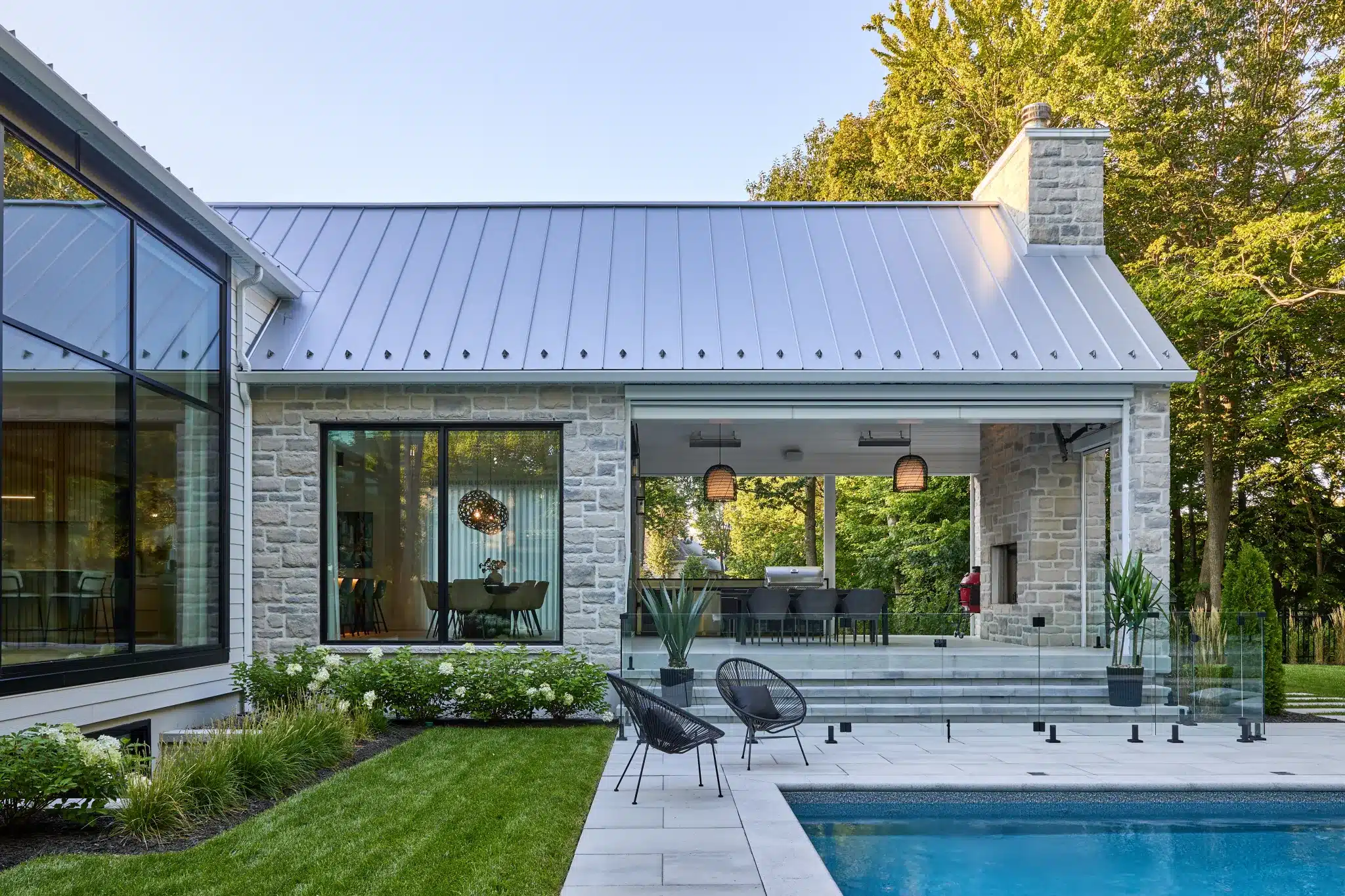 Façade arrière en maçonnerie claire avec terrasse couverte, espace repas extérieur et piscine au premier plan.