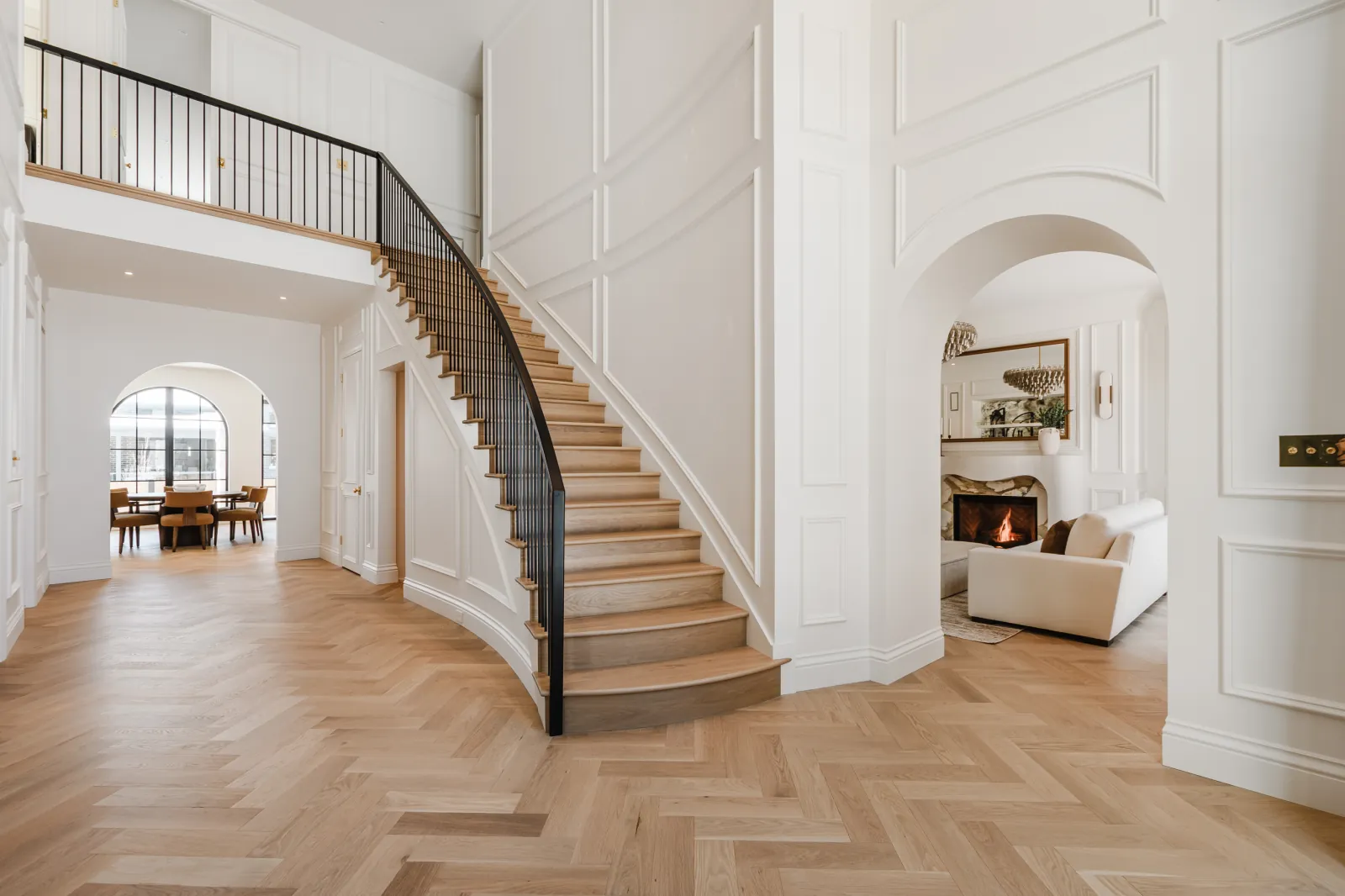 2508-alex-parent Escalier courbe dans un hall à double hauteur, avec une galerie à l’étage et des passages cintrés au rez-de-chaussée.