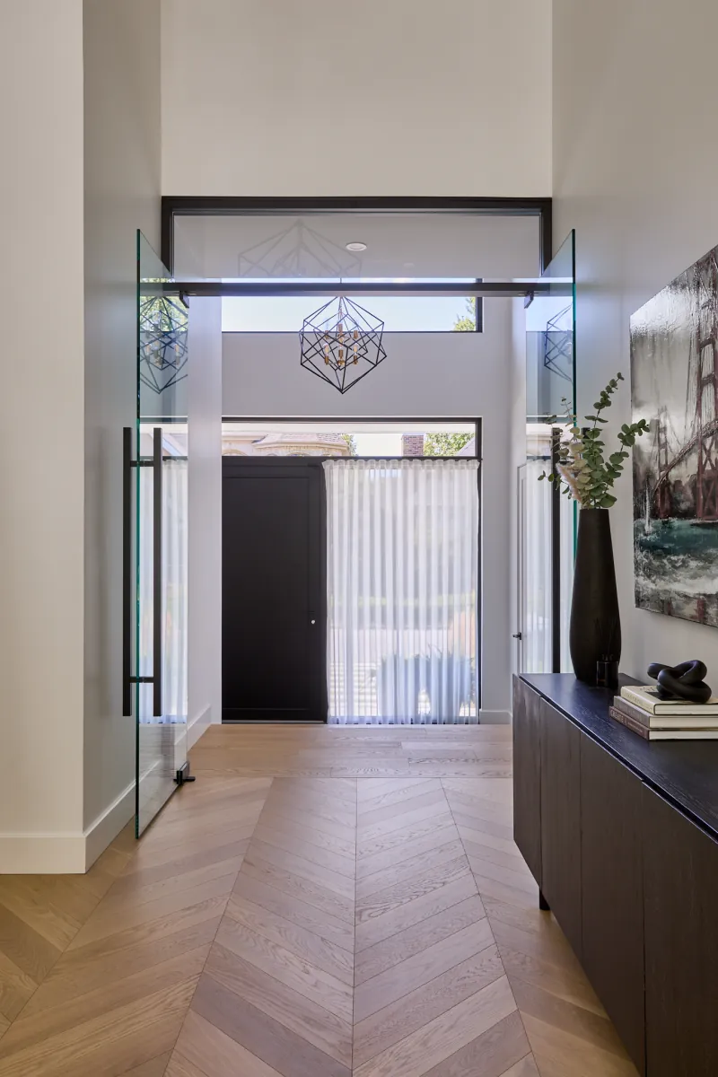 Entrée de la Maison S+J avec imposte vitrée, luminaire suspendu et plancher de bois à chevrons.