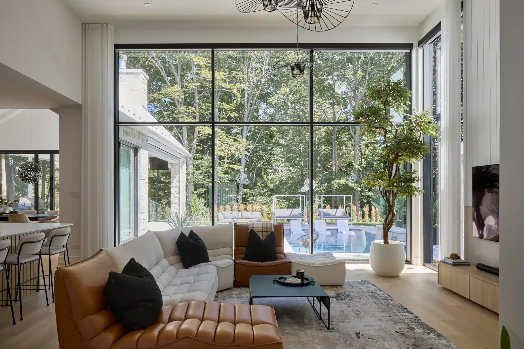 Salon avec canapé d’angle, grande fenestration et vue sur la piscine et la terrasse couverte.